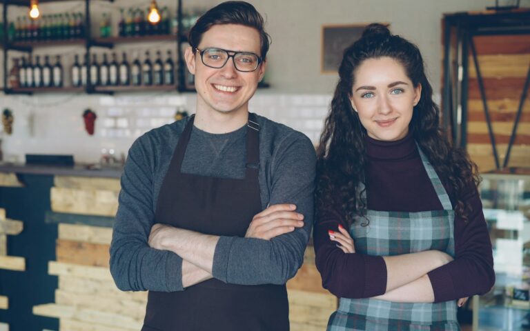 Dos dueños de una cafetería de pie delante de la barra de su negocio