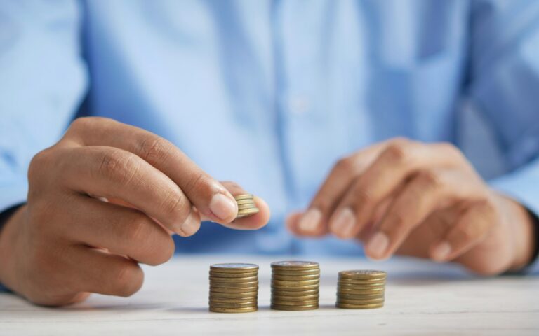 Manos apilando monedas en tres montones sobre una mesa