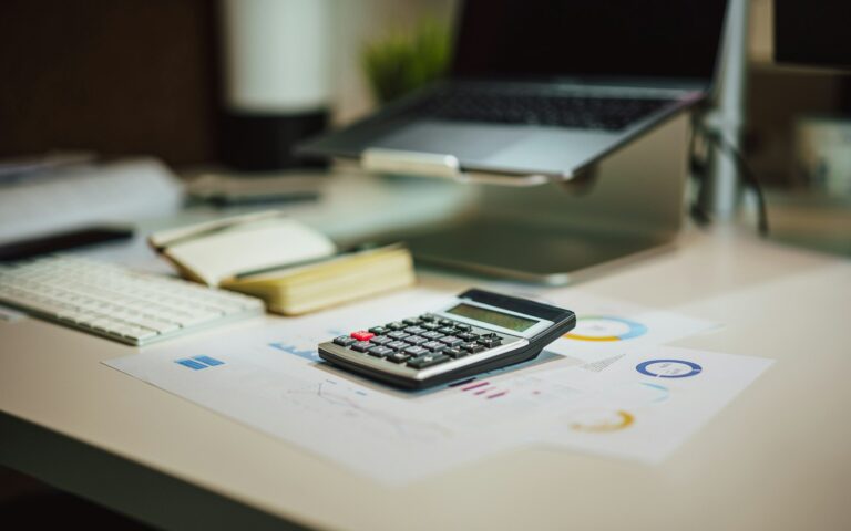 Calculadora y documentos con gráficos sobre un escritorio junto a un portátil