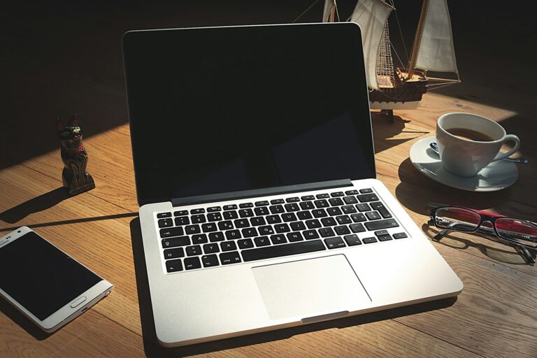 Un portátil abierto sobre una mesa de madera junto a una taza de café
