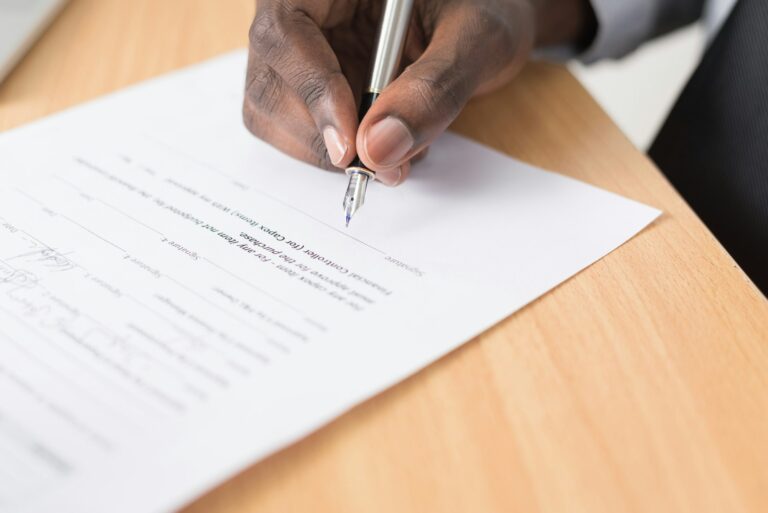 Una mano firma un documento con un bolígrafo sobre una mesa de madera