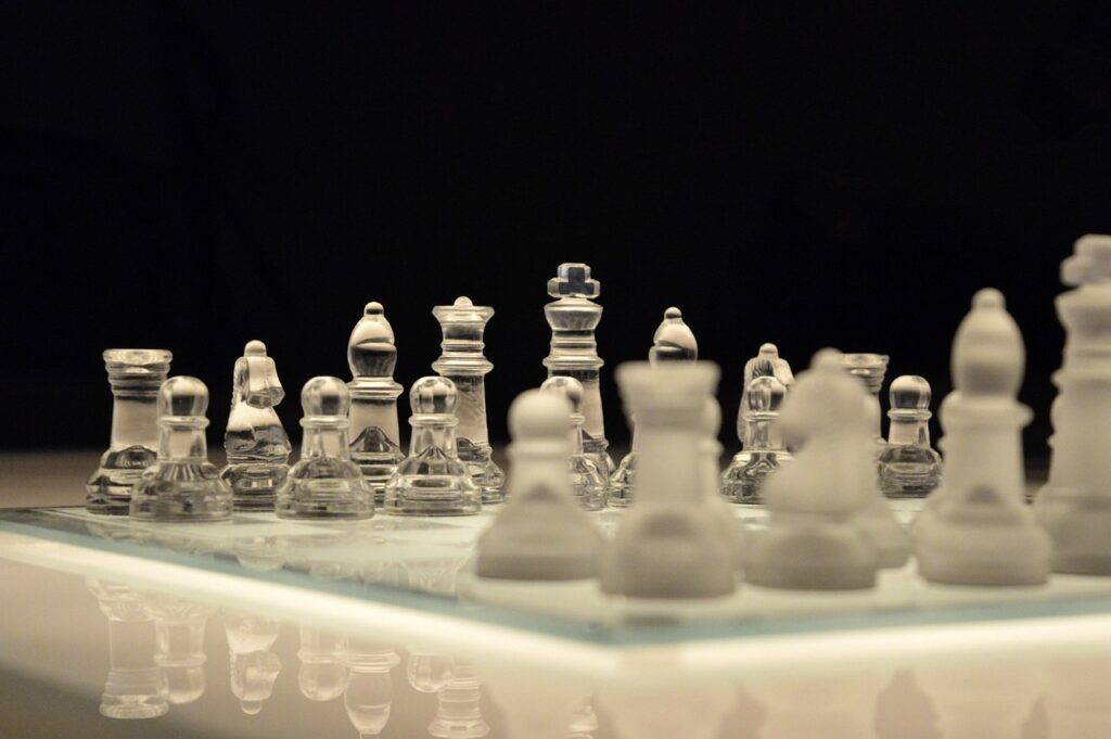 Piezas de ajedrez de cristal sobre un tablero de vidrio, con las blancas desenfocadas en primer plano y fondo negro