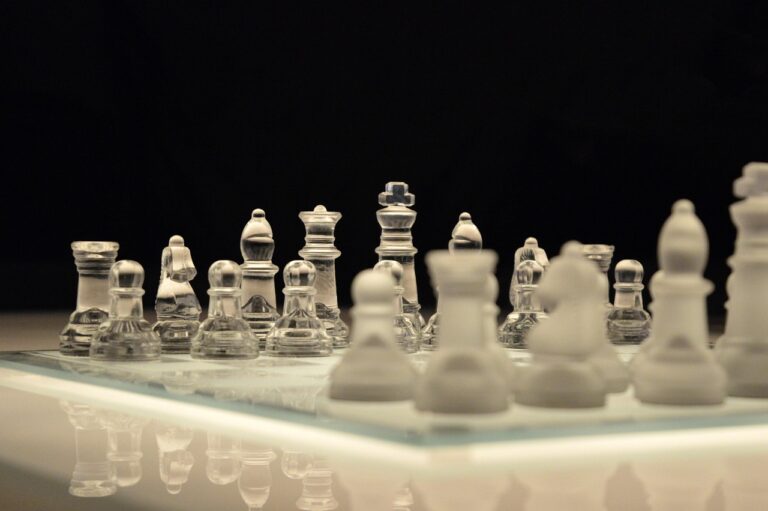 Piezas de ajedrez de cristal sobre un tablero de vidrio, con las blancas desenfocadas en primer plano y fondo negro